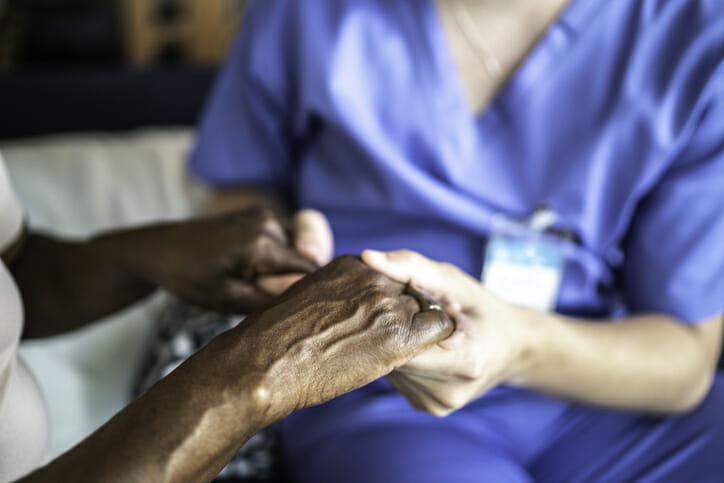 Long-term care staffing. A nurse and an elderly patient hold hands.