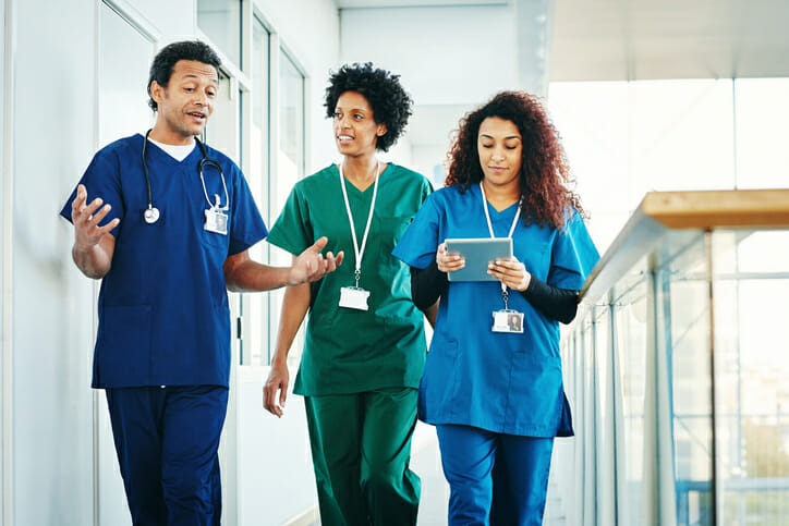 Ways to improve your company culture. Three healthcare workers walk down a hall together, smiling and talking.