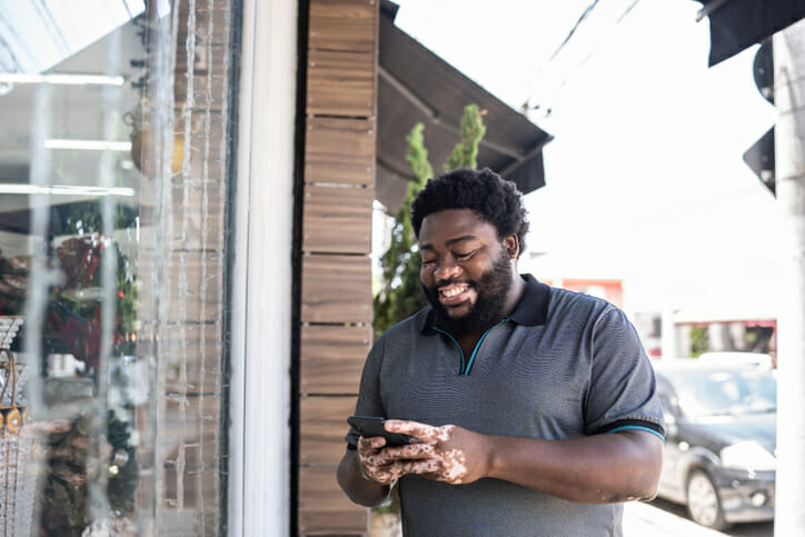 Define candidate experience. A man stands outside a storefront and smiles while looking at his phone.